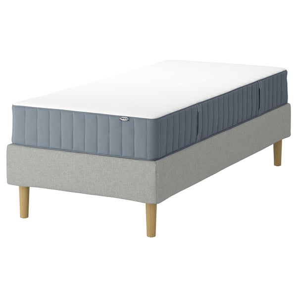 Bilden visar IKEA LYNGÖR grå sängbotten med träben och blå madrass.