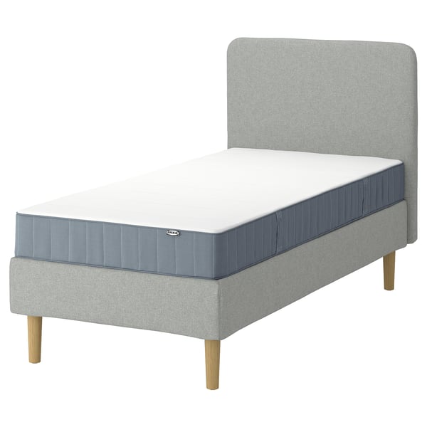 IKEA LYNGÖR säng: grå, modern, stoppad ram med ljusa träben, mjuk vit madrass, minimalistisk design.