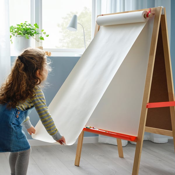 Ett barn vecklar ut ett stort ritpapper från ett trästaffli med en svart tavla och whiteboard, vilket främjar kreativitet och lärande.