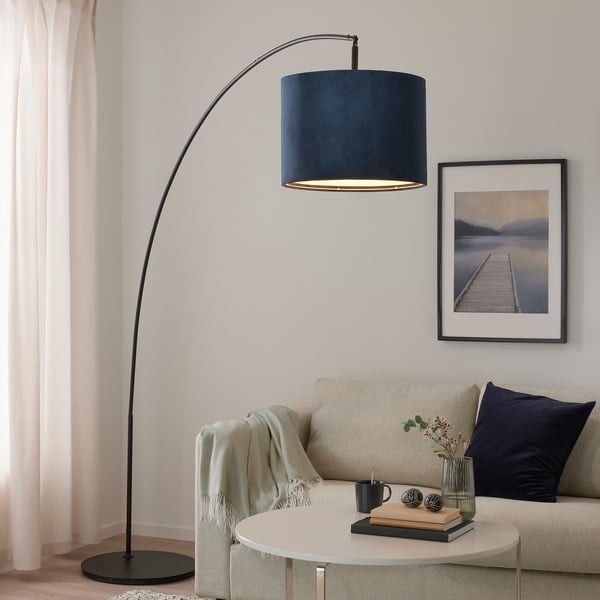 Modernt vardagsrum med hög, mörk lampa MOLNSKIKT som lyser upp en beige soffa och soffbord med inredning.