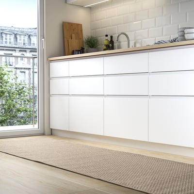 Modern kök med vit MORUM-matta , ljusa trägolv, flodbänkskivor och eleganta skåp vid fönstret.