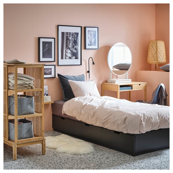 Mysigt sovrum med beige NORDLI-säng, med förvaringshyllor i trä till vänster och ett litet nattduksbord med en rund spegel.