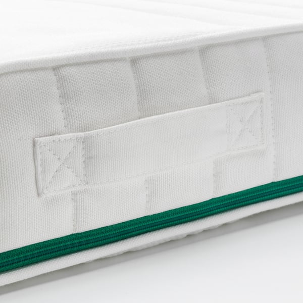 Närbild av högkvalitativ madrass som visar rena sömmar, vit quiltad design och grön kant, med betoning på hantverk och komfort.
