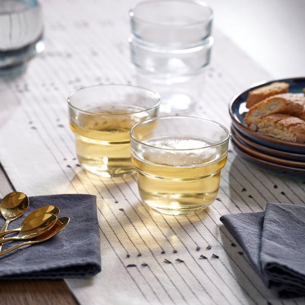 Tre glas fyllda med vätska på en randig trasa, åtföljda av en tallrik bröd och två skedar.