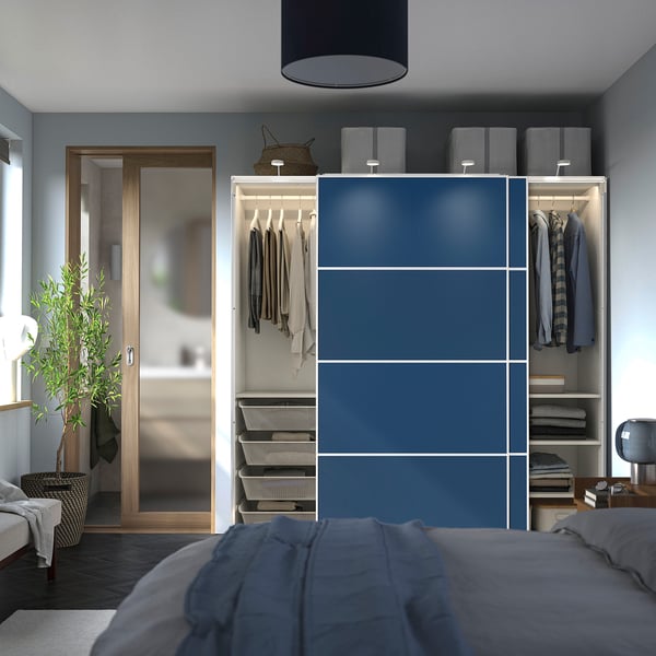 Modern sovrum med blå garderob med skjutdörrar, hängande kläder och hyllor.