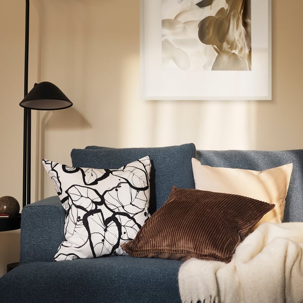 En mysig blå soffa med stor PELARKÖRSBÄR-kudde , svart lampa och abstrakt konst bakom.