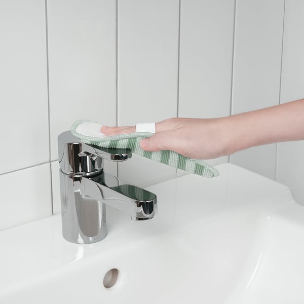 Personen rengör diskbänkens kran med en grön mikrofiberduk fäst vid det utdragbara handtaget.