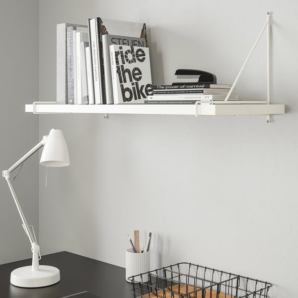 Vit PERSHULT hyllkonsol med böcker och lampa. Skrivbordet har pennhållare och trådkorg.