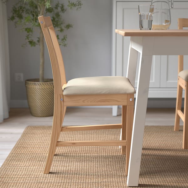 Modern trästol med vinklad rygg och vadderad sits, perfekt för matkomfort. Beläget nära ett bord med naturliga inredningselement.