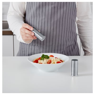 Person som kryddar pasta med pepparkvarn. Skål med pasta med tomater i närheten.