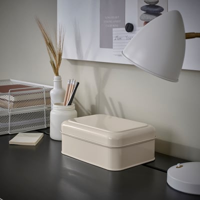 Liten vit PLOGFÅRA-låda på ett skrivbord, bredvid en lampa och pennor. Organizer passar bra med andra skrivbordsartiklar.