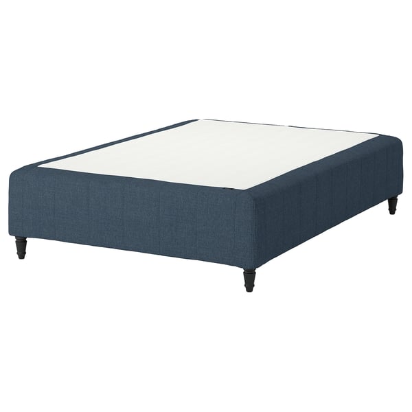 På den här bilden står sängbottnen IKEA RÅHOLMAR i mörkblått, med en rektangulär form och fyra ben i trä. Den stöder en vit madrass.