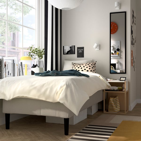 Minimalistiskt sovrum med sängen RÅHOLMAR , vit madrass, svarta ben, stilren inredning, naturligt ljus.