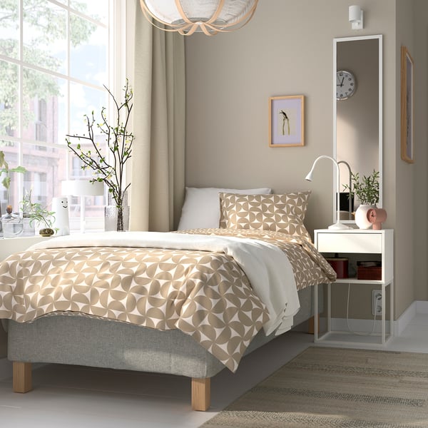 Modern säng med geometriskt tryckt täcke, två nattduksbord med lampor och en stor spegel som passar perfekt in i ett väl upplyst, minimalistiskt sovrum.