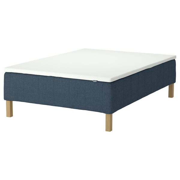 En IKEA RÅHOLMAR sängbotten i mörkblått med ljusa träben. Det är en vit madrass med minnesskum.