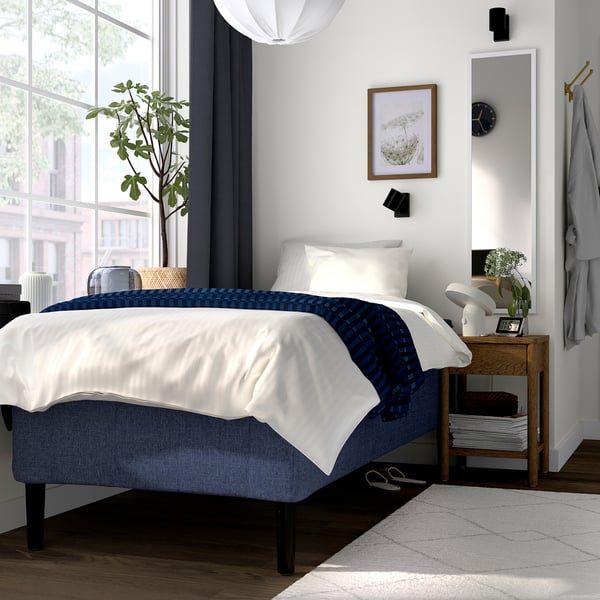 Minimalistiskt sovrum med sängen RISHÖJDEN , blåvita sängkläder, växt och klocka.