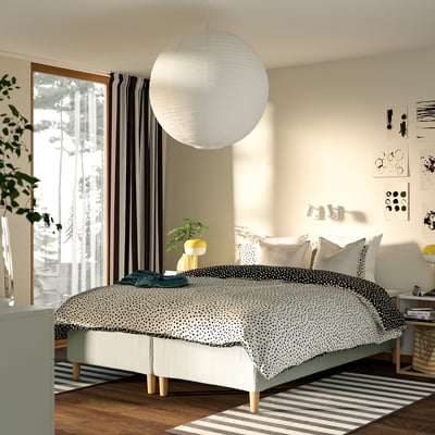 Modern sovrum med stor säng, prickiga sängkläder, randiga gardiner, pendellampa och trägolv.