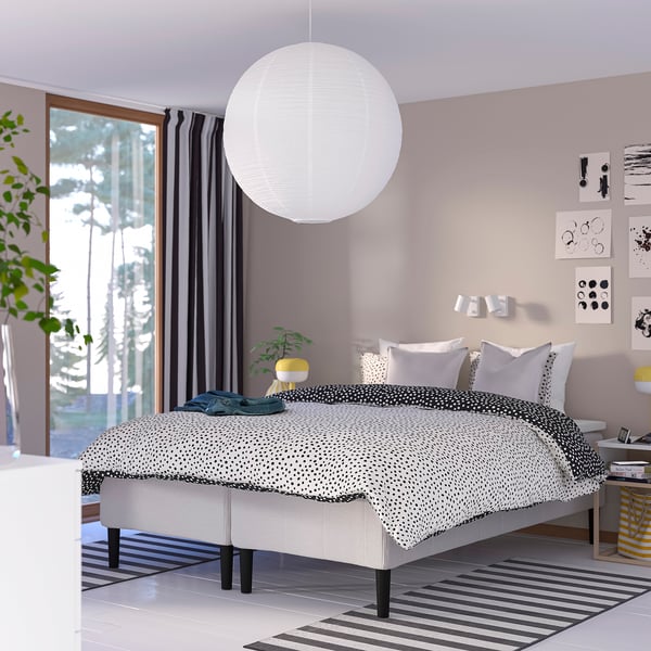 Modern sovrum med stor säng, pendellampa, skrivbord och fönster.