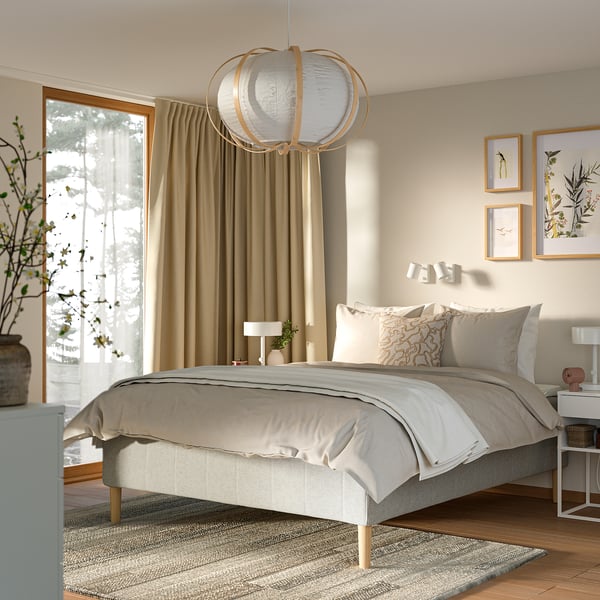 Modern sovrum med vit säng, beige gardiner, unik hänglampa, väggkonst och trägolv; Mysigt och minimalistiskt.