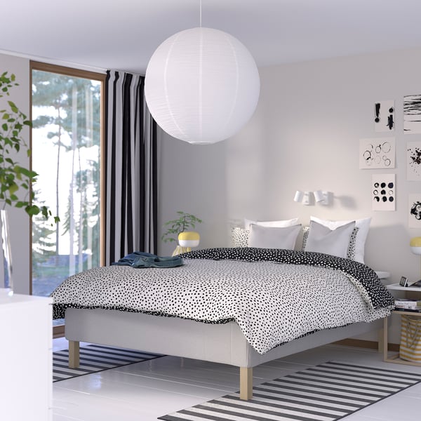 Modernt sovrum med sängen RISEHÖJDEN , svarta gardiner, taklampa, randig matta, växt, lampa, konst, balkong.