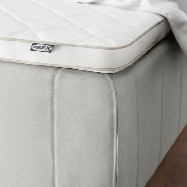 En närbild av ett hörn på en vit IKEA RISHÖJDEN-madrass med vadderad kant, som visar dess förstärkta kantdesign för stabilitet och stöd.