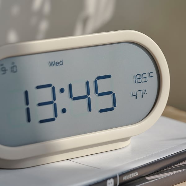 Modern klocka visar tid, temperatur, luftfuktighet – slank, vit design.