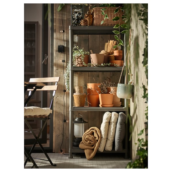 Inomhus och utomhus metallhyllor med krukväxter, kuddar och en lykta, som visar en rustik design.