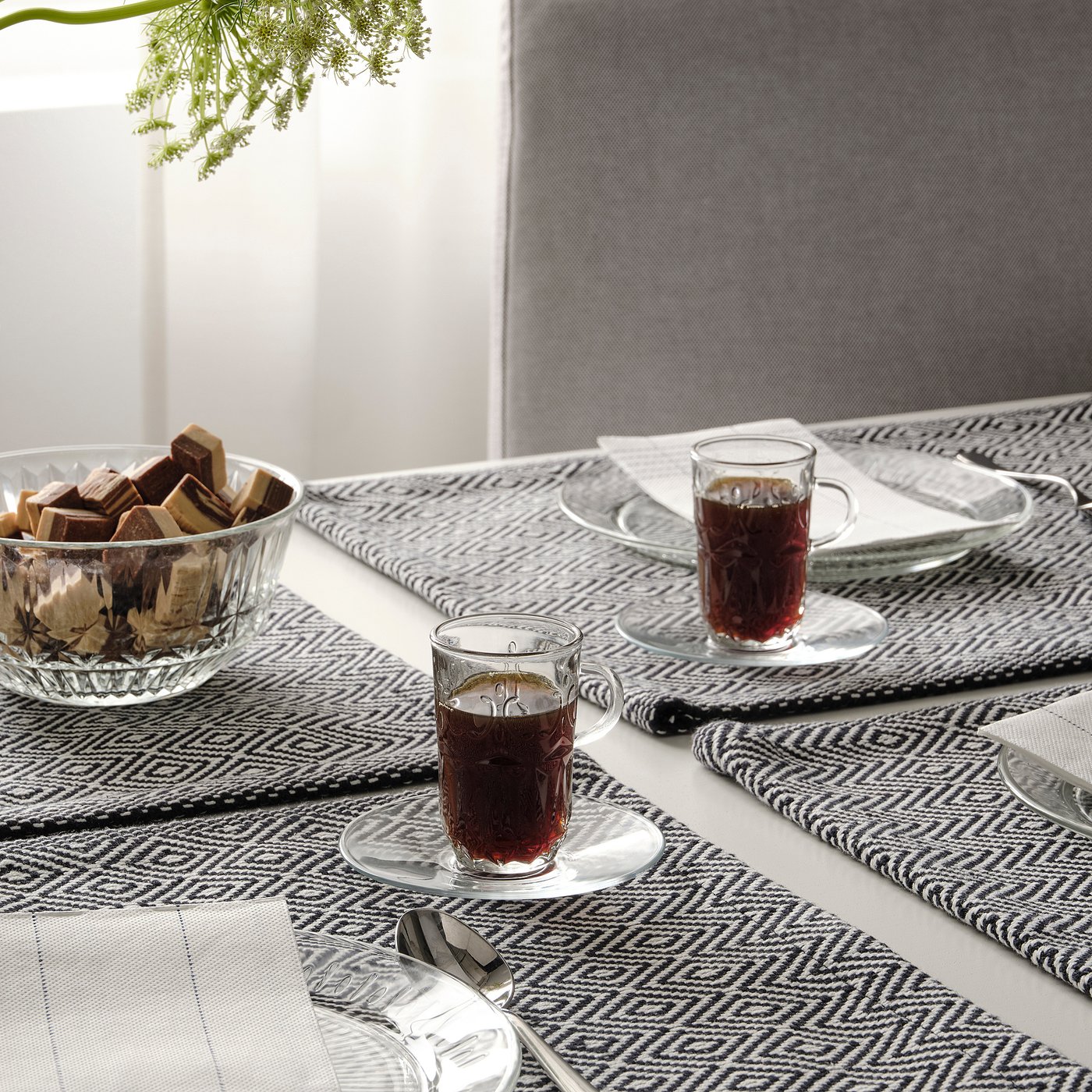 Bordsdukning med SÄLLSKAPLIG glas, koppar och fat; skål med choklad, servetter och bestick.
