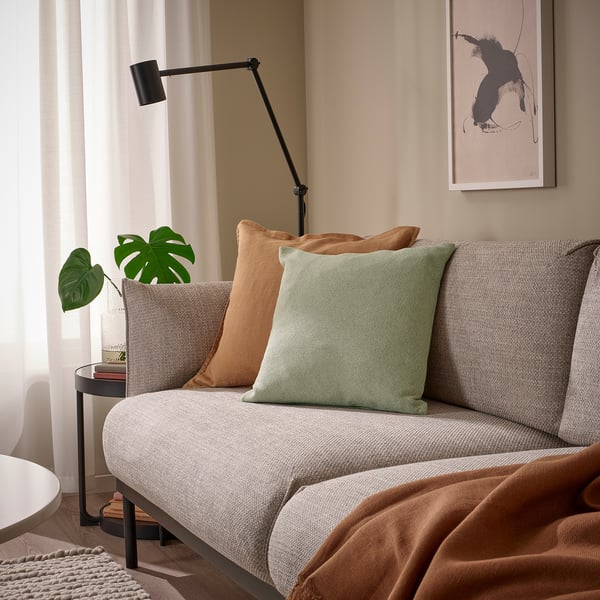 Modernt vardagsrum med ljus soffa, färgglada kuddar, väggkonst, lampa, växt och böcker.