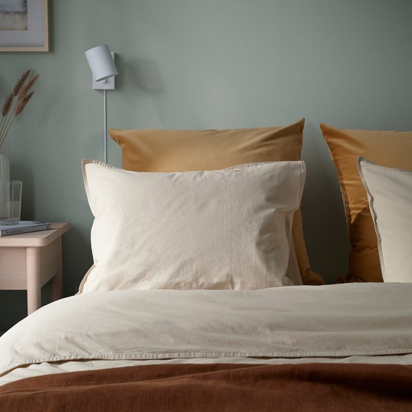 Mysigt sovrum med stora bruna sammetskuddar, beige sängkläder och minimalistiskt nattduksbord med lampa.
