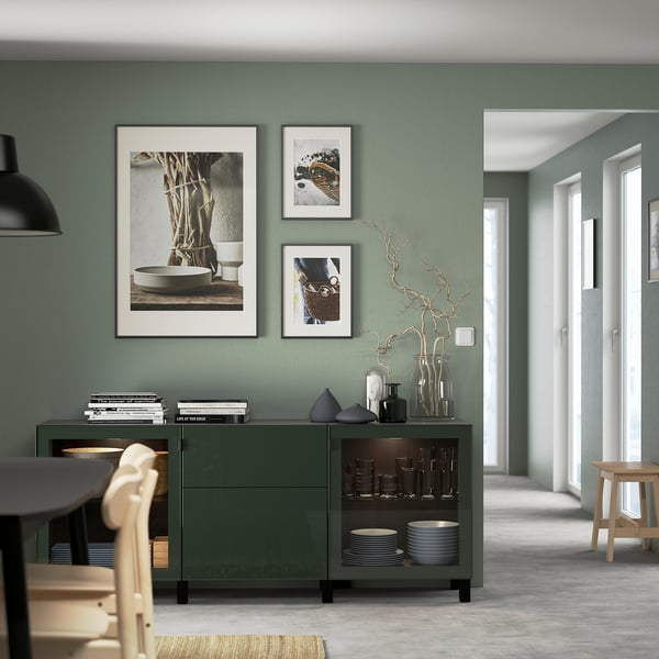 Modern matsal med olivgrönt sideboard, konst och trästolar. Perfekt placerad mellan grå vägg och bord, med porslin.