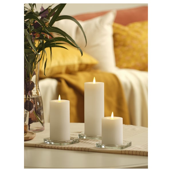 Tre vita IKEA SILVERMÅS ledljus i olika höjder på ett bord med en gul prydnadskudde i bakgrunden.