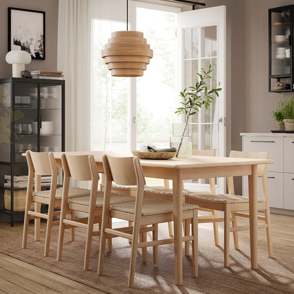 Modern matgrupp i ljust trä med utdragbart bord, fyra matchande stolar, taklampa och dekorativa tillbehör.