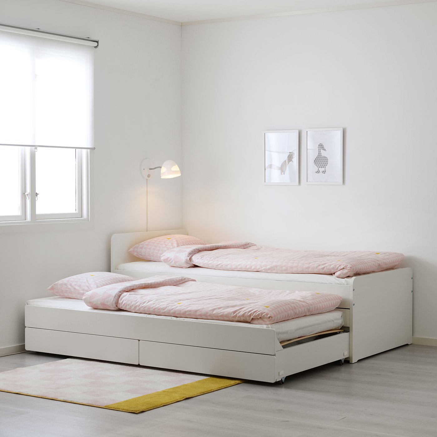 Ljusvit SLÄKT dubbelbädd med rosa lakan och väggmonterad läslampa, små ramar, lätt matta, enkel, minimalistisk design, passar bra i små rum.