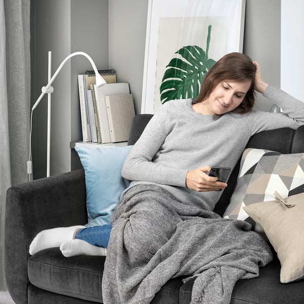 Kvinnan kopplar av på retro soffa med telefon, mysig filt, kuddar, i modernt rum med böcker, växter.