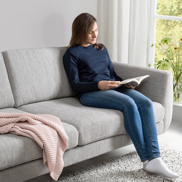 Kvinnan läser bok på mysig soffa med armstöd, texturerat tyg och konben.
