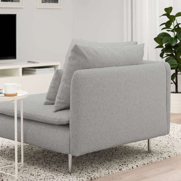 En modern, ljusgrå soffa med dynor på en spräcklig matta. Soffan är designad med höga ben och djupa sitsar för komfort.