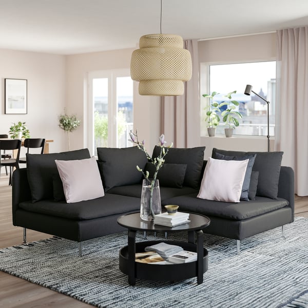 Modernt vardagsrum med stor svart SÖDERHAMN sektionssoffa, elegant soffbord, snygg taklampa och stora fönster med utsikt över staden.