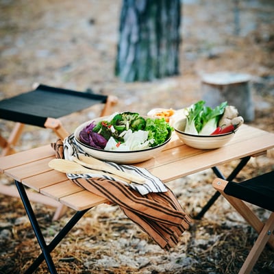 Bambuskålar med grönsaker på campingbordet, naturbakgrund.