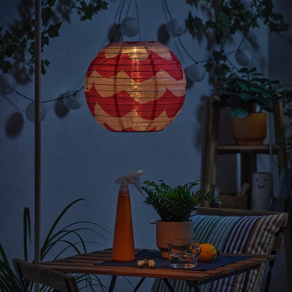 Mörk uteplats med röd lykta. Bordet har växt, glas, citron. Glödande lykta.
