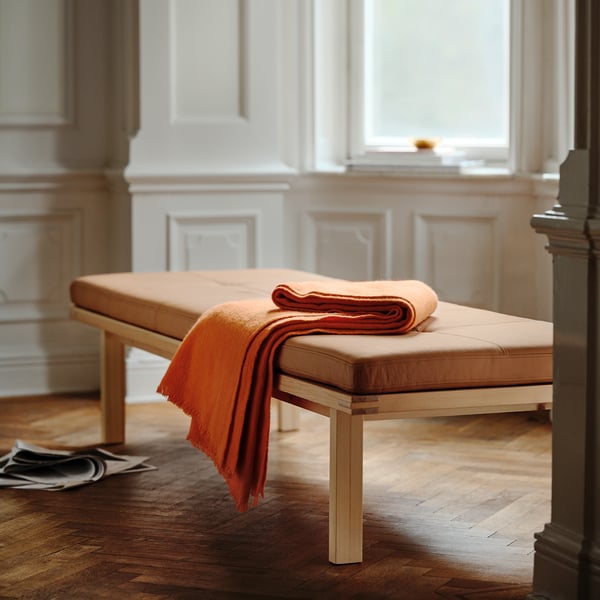 På den här bilden finns en stockhom 2025 bänk i orange läder, med en ram i massivt trä. Dess stora, väldämpade och eleganta, moderna skandinaviska design.