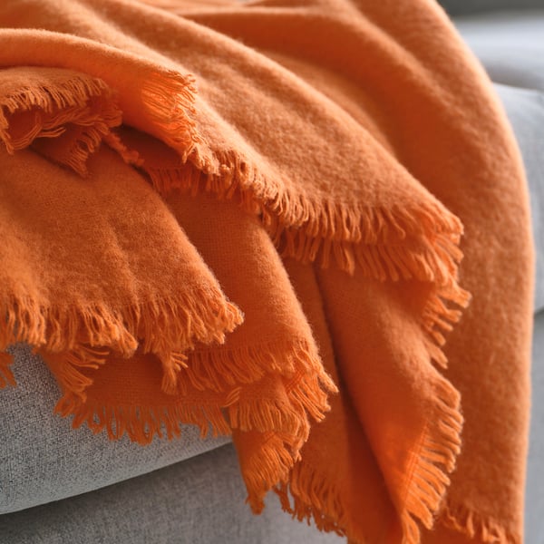En knallorange filt som är snyggt vikt och visar upp ett mjukt, strukturerat ullmaterial med franskanter.
