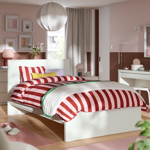 Modern vit säng med rödvita ränder, pendellampa, konst, rosa lampa, gardiner, matta, tofflor.