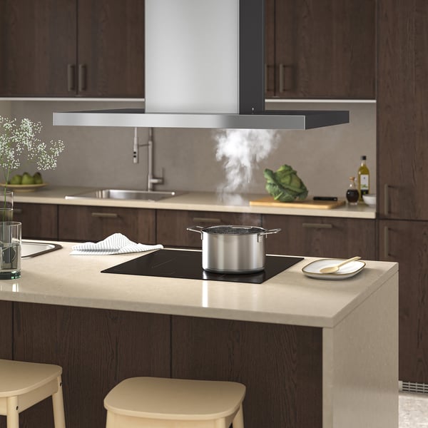 Modernt kök med spisfläkt, LED-lampor och ångande kastruller. Beige bänkar, träskåp och pallar.