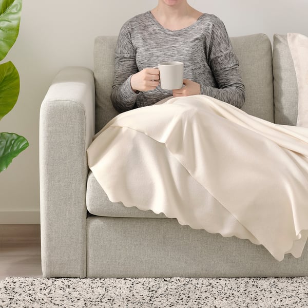 Person som sitter på soffan med filten, håller koppen.