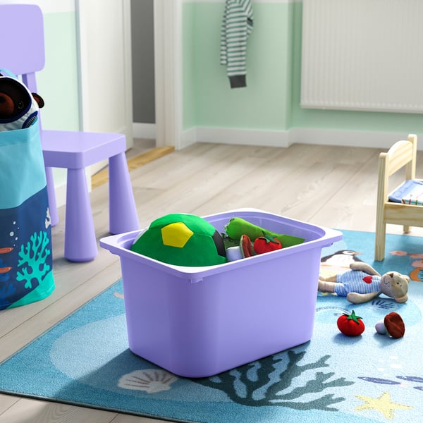 Lila TROFAST leksaksbehållare rymmer barnleksaker på en blå matta nära en liten stol.