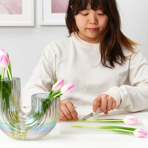 Ung kvinna som ordnar rosa tulpaner i en u-formad vas av glas och klipper stjälkarna med sax.