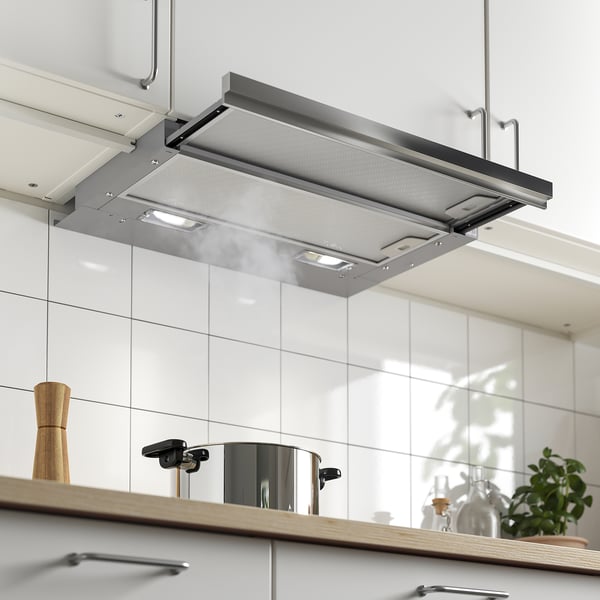 Spis fläkt i rostfritt stål inbäddad i vitt köksskåp, upplyst med LED-lampor, som visar dess extraherade tillstånd.