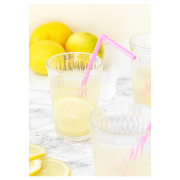 Två glas med citronsaft och rosa sugrör står på ett marmorbord, omgivna av citroner.
