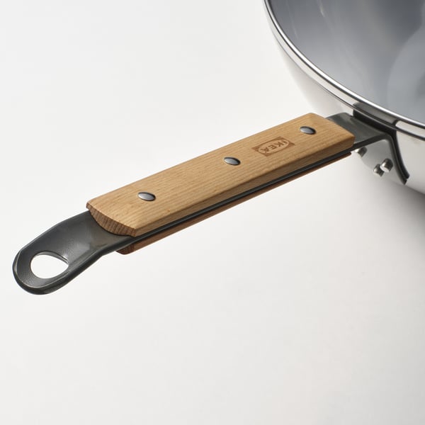 Närbild av ett robust wokhandtag med trägrepp och metallögla, säkert fixerat med skruvar, som visar en robust design på en ren vit bakgrund.
